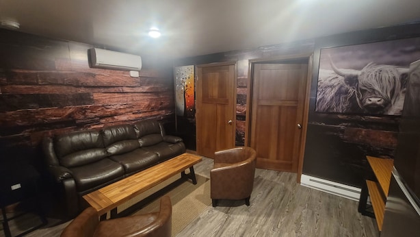 Una habitación acogedora con un sofá de cuero, un banco de madera, una mesita y una puerta.