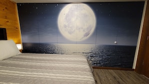 Un dormitorio con una cama grande, cabecera de madera y un mural en la pared que muestra la luna sobre el mar.
