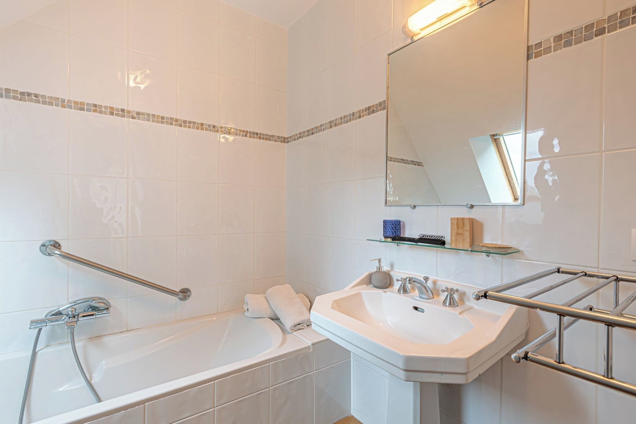 Ein Badezimmer mit Badewanne, Waschbecken, Spiegel und Handlauf.