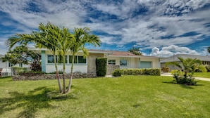 A single-story house with a stone foundation, a light blue exterior, and a red roof. - Villa Tropical Vibes - Charming 3 BR waterfront Villa with heated pool, bicycles, fishing poles - walking distance to bars and restaurants (Cape Coral)