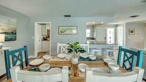 A dining area with a wooden table set for four, surrounded by white chairs with blue accents. A potted plant is in the center of the table. - Villa Tropical Vibes - Charming 3 BR waterfront Villa with heated pool, bicycles, fishing poles - walking distance to bars and restaurants (Cape Coral)