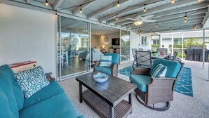 An outdoor living area with wicker furniture, a glass wall, and string lights. - Villa Tropical Vibes - Charming 3 BR waterfront Villa with heated pool, bicycles, fishing poles - walking distance to bars and restaurants (Cape Coral)