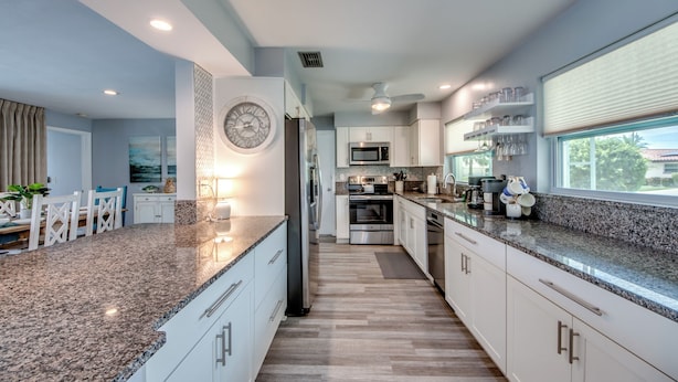 A modern kitchen with granite countertops, stainless steel appliances, and a dining area with a table and chairs. - Villa Tropical Vibes - Charming 3 BR waterfront Villa with heated pool, bicycles, fishing poles - walking distance to bars and restaurants (Cape Coral)
