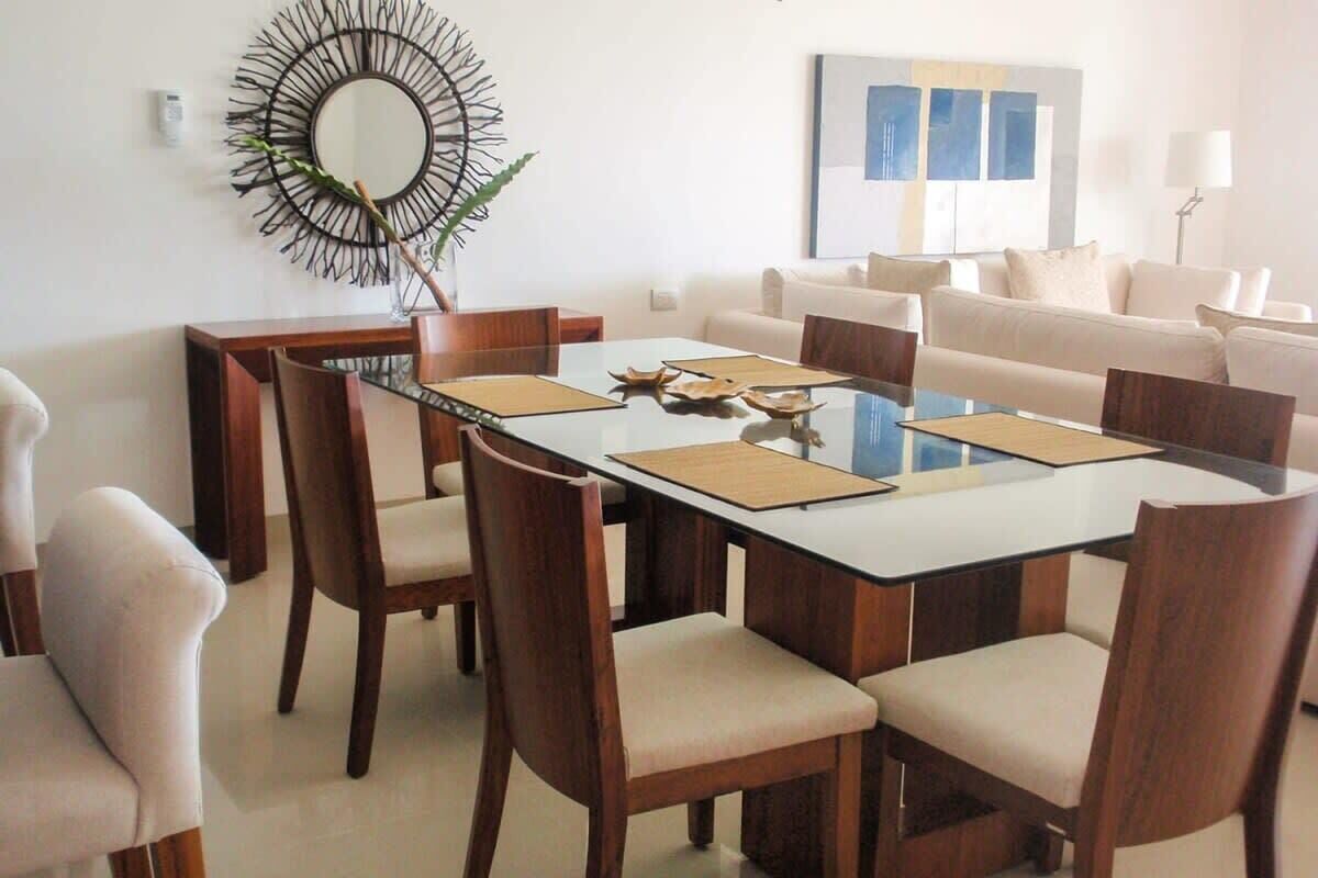 Un espace repas moderne avec une table à plateau en verre, des chaises en bois et un miroir décoratif au mur.