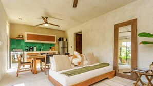 A bedroom with a bed, a wooden bedside table, a ceiling fan, and a view of the kitchen. - Jungle-View Rooftop Retreat | La Veleta Sanctuary (Tulum)