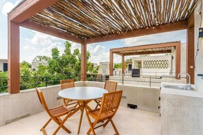 Eine Außenpatio mit einem runden Tisch und Stühlen, einem darüberliegenden Pergola und Blick auf Gebäude im Hintergrund.