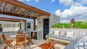 An outdoor patio with a wooden table and chairs, a sofa with patterned cushions, and a potted plant. - Jungle-View Rooftop Retreat | La Veleta Sanctuary (Tulum)