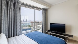 Ein Hotelzimmer mit einem großen Bett, einem Fernseher und Blick auf eine Stadtlandschaft durch ein großes Fenster.