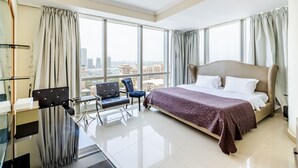 Ein Hotelzimmer mit einem großen Bett, einem Schreibtisch, zwei Stühlen und Blick auf die Stadt durch große Fenster.