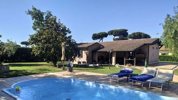 Piscina com espreguiçadeiras e um terraço coberto.