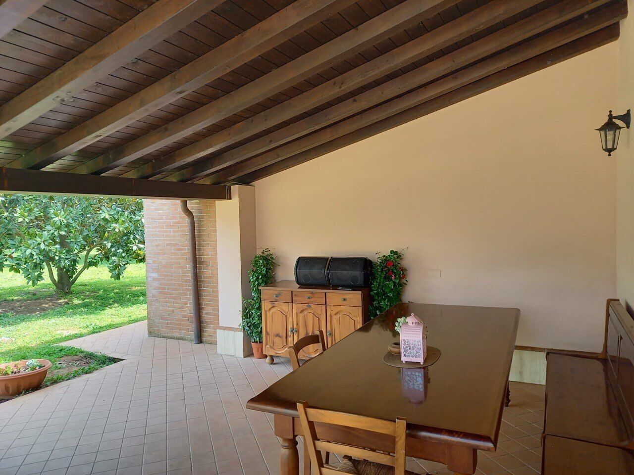 Patio esterno con tavolo e sedie di legno, un muro in mattoni e un barbecue.