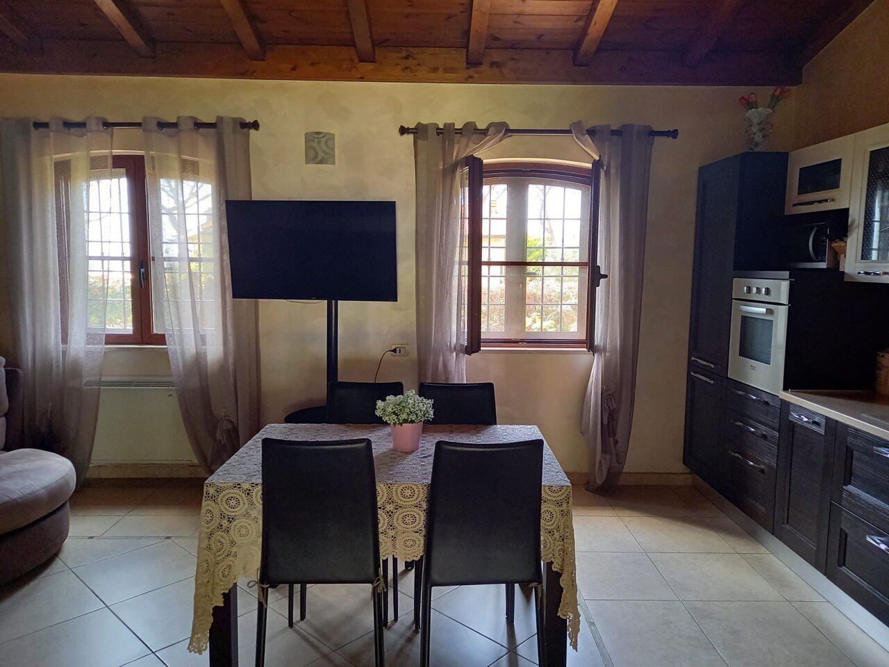 A dining area with a table, chairs, a flat-screen TV, and a kitchen with appliances.