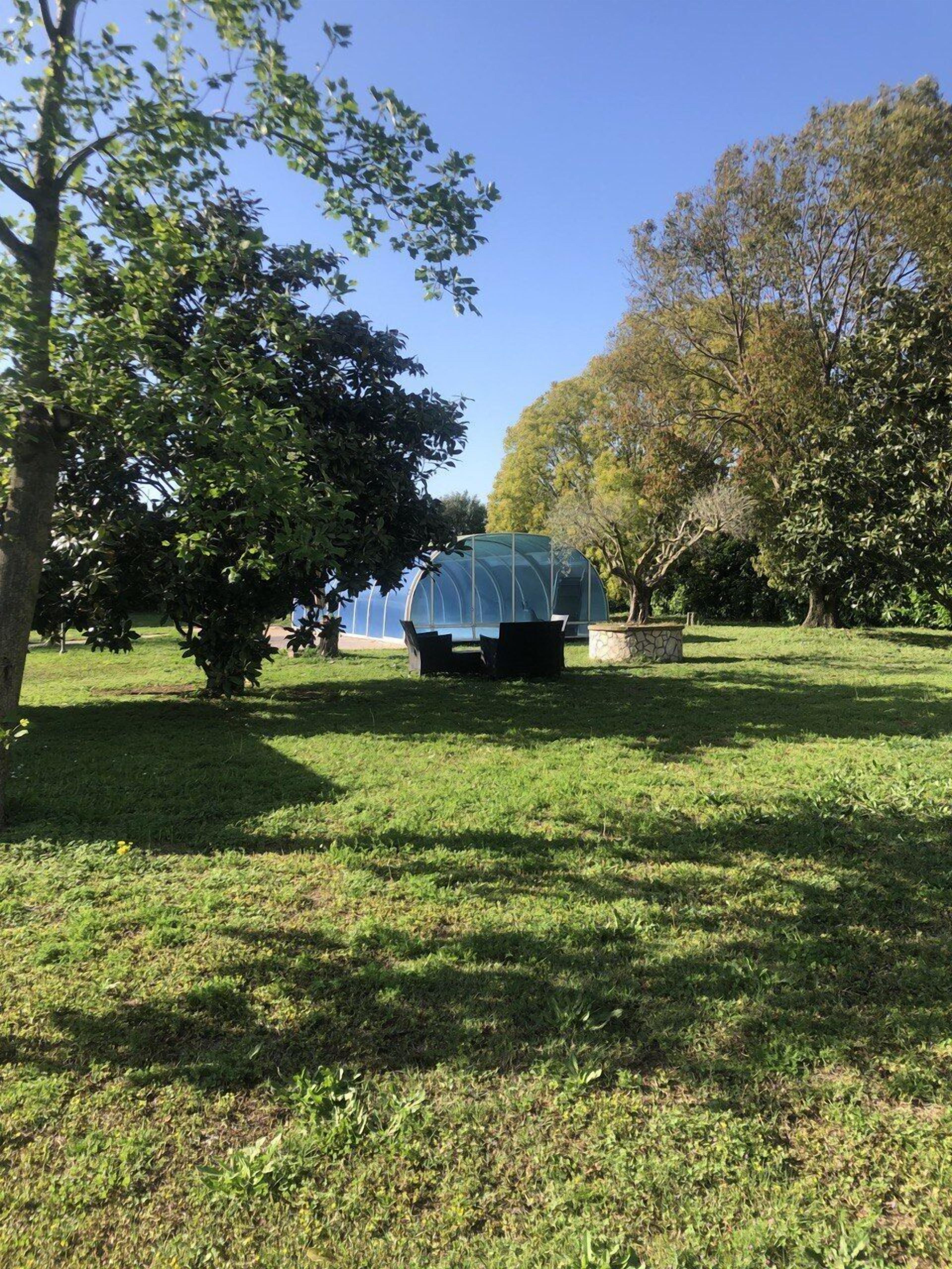 A greenhouse structure in a park with grass and trees around.