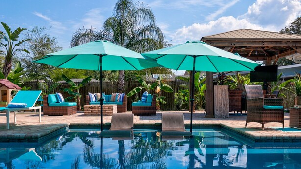 Un espace piscine aménagé avec des chaises longues, des parasols et des meubles en osier.