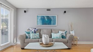 Un salon avec un canapé gris, une table basse blanche et un tableau abstrait bleu accroché au mur.