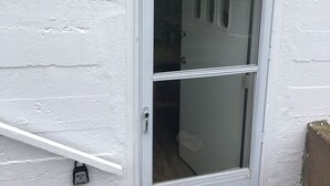 Une porte extérieure blanche, dotée d’une poignée en métal, d’un judas et d’un panneau d’avertissement.