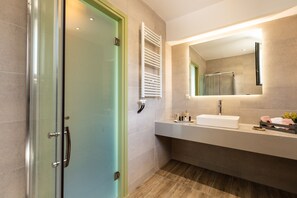 Ein modernes Badezimmer mit Duschabtrennung aus Glas, einem weißen Waschbecken und einem Spiegel mit integrierter Beleuchtung.