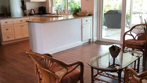 A spacious kitchen with a central island, wooden flooring, and a dining area with wicker chairs and a glass table. - Lovely House on the canal with private dock, large fenced yard & pet friendly (Apollo Beach)