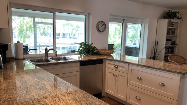 A kitchen with granite countertops, white cabinetry, a dishwasher, and a clock on the wall. - Lovely House on the canal with private dock, large fenced yard & pet friendly (Apollo Beach)