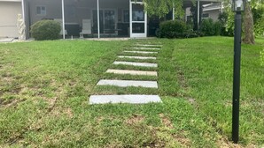 A pathway leading to a building with a covered entrance, a lawn, and a tree. - Lovely House on the canal with private dock, large fenced yard & pet friendly (Apollo Beach)