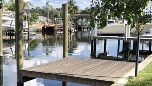 A wooden dock extending into calm water, surrounded by boats and greenery. - Lovely House on the canal with private dock, large fenced yard & pet friendly (Apollo Beach)