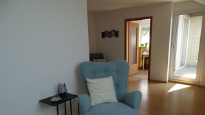 Een woonkamer met een blauwe fauteuil, een klein tafeltje met een glas, en een deur die uitkomt op een balkon.