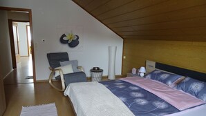 Een slaapkamer met een bed, een schommelstoel, een klein nachtkastje en een wandlamp.