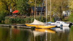 Een rustig meer met aangemeerde boten, een restaurant met terras en een traditioneel gebouw op de achtergrond.