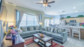 A modern living room with a sectional sofa, a coffee table, and a dining area with a white table and chairs. - Lakefront Windsor Hills - 6 Bed 4 Bath Home with Custom Mickey Mouse Heated Pool (Kissimmee)