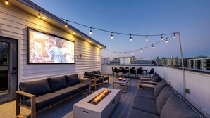 A rooftop terrace with a fire pit, outdoor seating, and a large TV screen. - Amplify - Rooftop cinema & city views (Nashville)