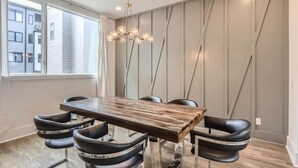 Ein Essbereich mit einem Holztisch, schwarzen Stühlen, einer modernen Chandelüster und Blick auf Gebäude durch große Fenster.