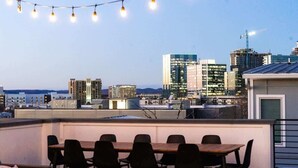 A rooftop terrace with a dining table and chairs, overlooking a cityscape with modern buildings and a construction crane. - Broadview - Rooftop fire pit & skyline views (Nashville)