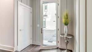 A hallway with a white door, a glass door leading outside, and a small table with a vase. - Broadview - Rooftop fire pit & skyline views (Nashville)