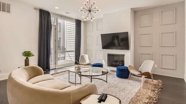 A modern living room with a sofa, chairs, a glass coffee table, a fireplace, and a TV mounted on the wall. - Broadview - Rooftop fire pit & skyline views (Nashville)