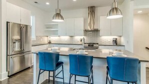 A modern kitchen with stainless steel appliances, a central island with bar stools, and pendant lighting. - Broadview - Rooftop fire pit & skyline views (Nashville)
