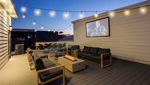 Eine Terrassenausstattung mit Feuerstelle, Sitzgelegenheiten und einer Projektionsleinwand.