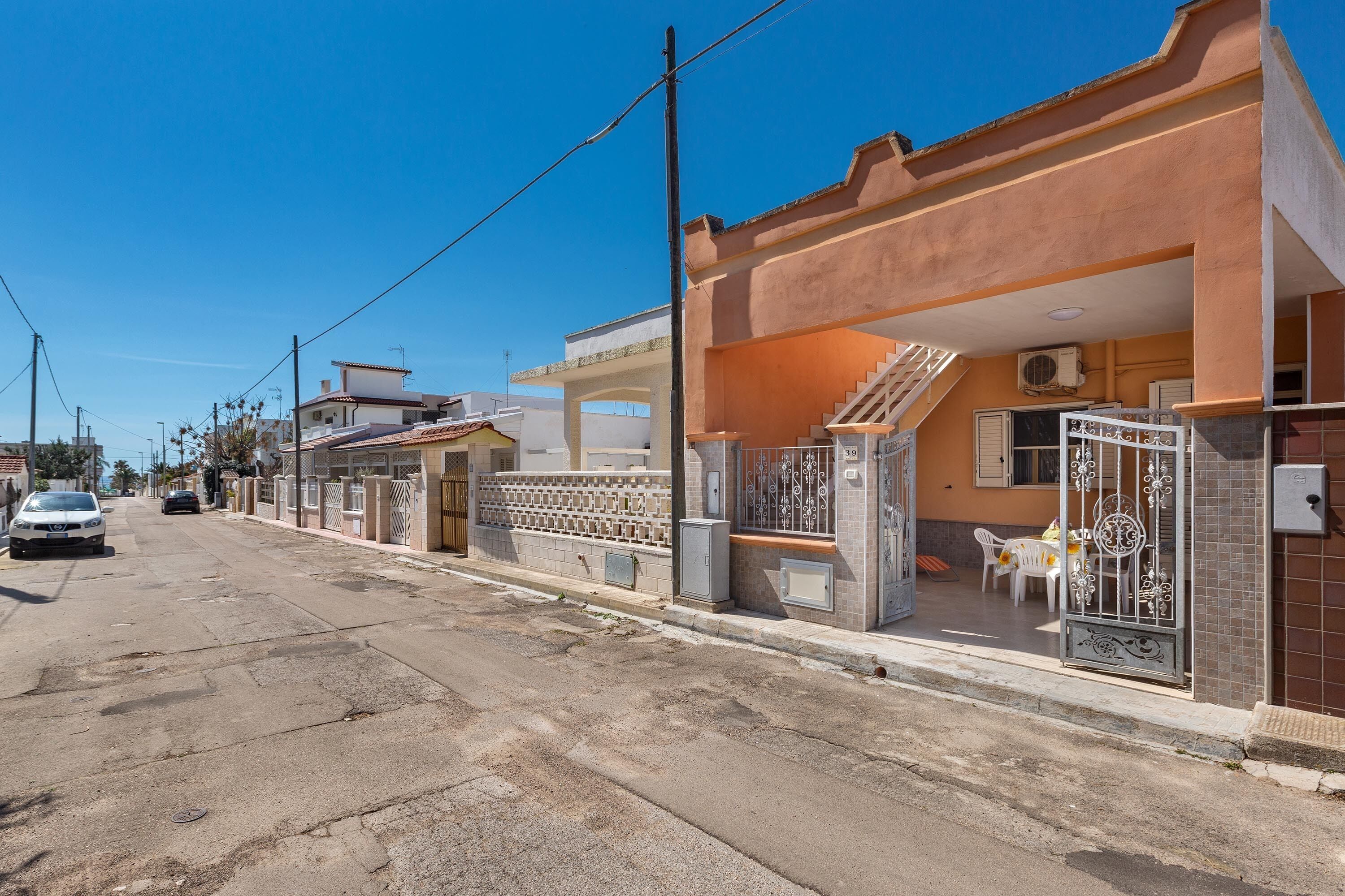 A residential street with houses, a parked car, and a gated entrance.