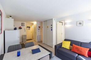 Een compacte leefruimte met een eethoek, een bank met decoratieve kussens en een koelkast.
