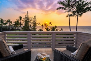 A balcony with wicker furniture and a view of the sunset over the ocean.
