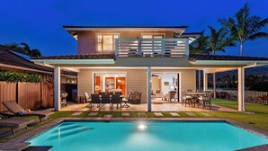 Una casa de dos pisos con piscina, mobiliario exterior y un porche cubierto.