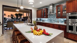 Una cocina moderna con una isla grande, armarios de madera y vista a palmeras.