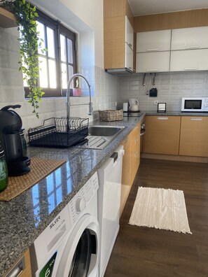 Cozinha moderna com máquina de lavar embutida, pia, micro-ondas e armários de madeira.