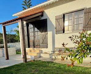 Uma casa com varanda, porta de madeira e janela com persianas.