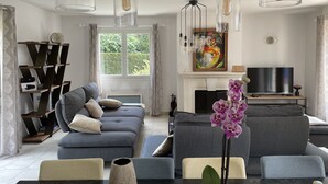 A modern living room with a grey sofa, a dining table with chairs, a fireplace, and pendant lights.