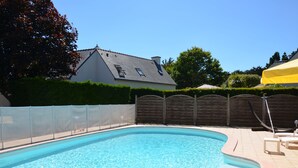 A swimming pool with a tiled deck, a wooden fence, and a house in the background.