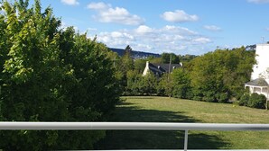 A balcony with a view of a grassy area, trees, and houses in the distance. - Appartement Avec Terrasses, Équipements Entièrement Neufs (Crozon)