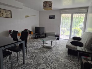 Un salon comprenant un téléviseur, une table à manger, des chaises, un sol à motifs et un canapé avec des coussins.