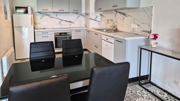 A modern kitchen with a marble backsplash, a built-in oven, a sink, and a dining area with two chairs. - Appartement Avec Terrasses, Équipements Entièrement Neufs (Crozon)