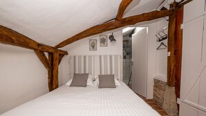 Une chambre avec un grand lit, des poutres apparentes, un sol carrelé et une porte blanche.