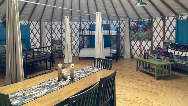 A spacious tent with a wooden floor, bunk beds, a dining table with candles, and a bear-themed wall decoration. - Pet-Friendly Yurt Sleeps 12 with Pool Access (Granville)